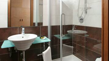 Un baño moderno con ducha de vidrio, lavamanos blanco y repisa de vidrio.