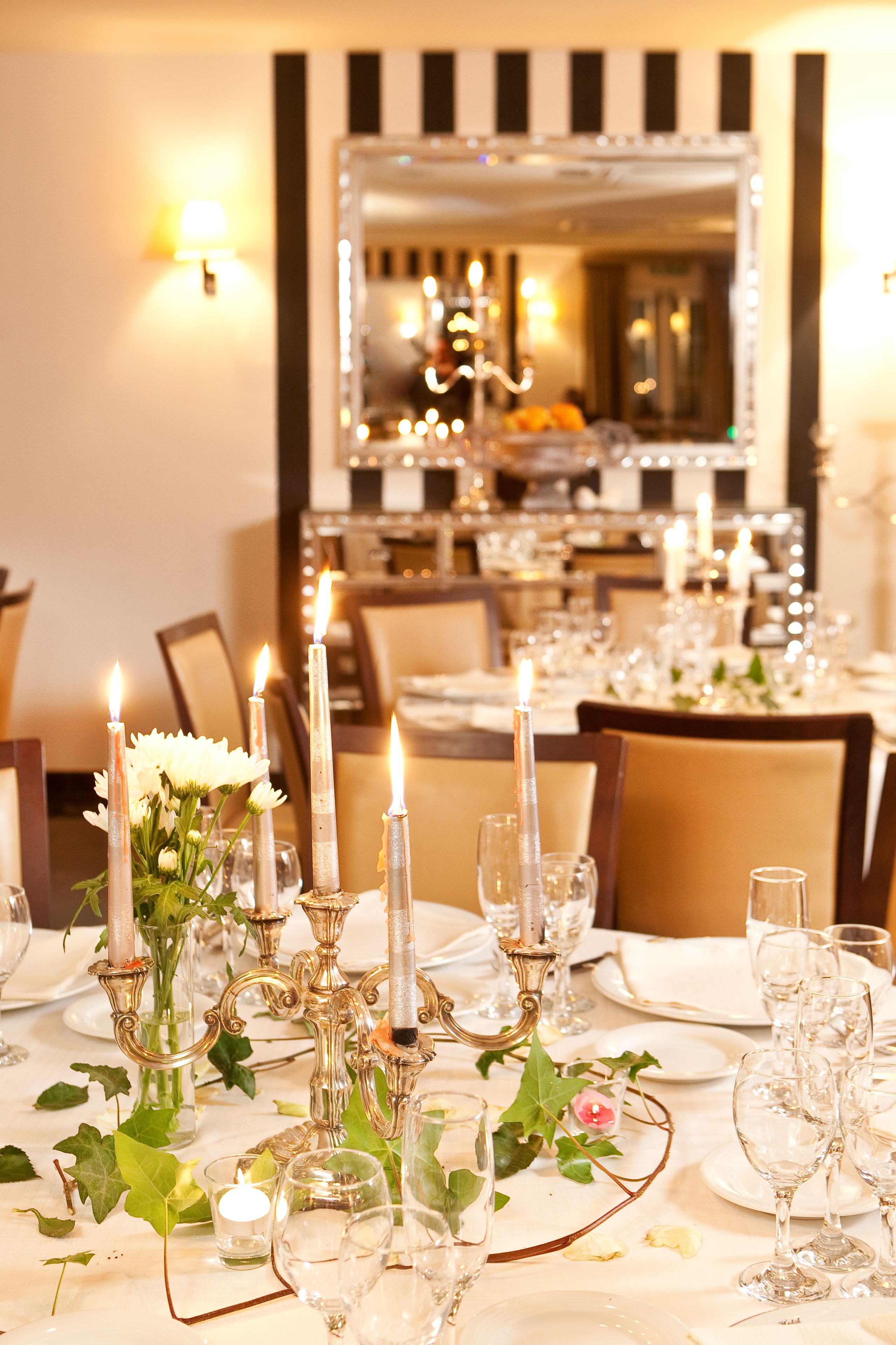 Une table à manger décorée avec des bougies, de la verrerie et des compositions florales.