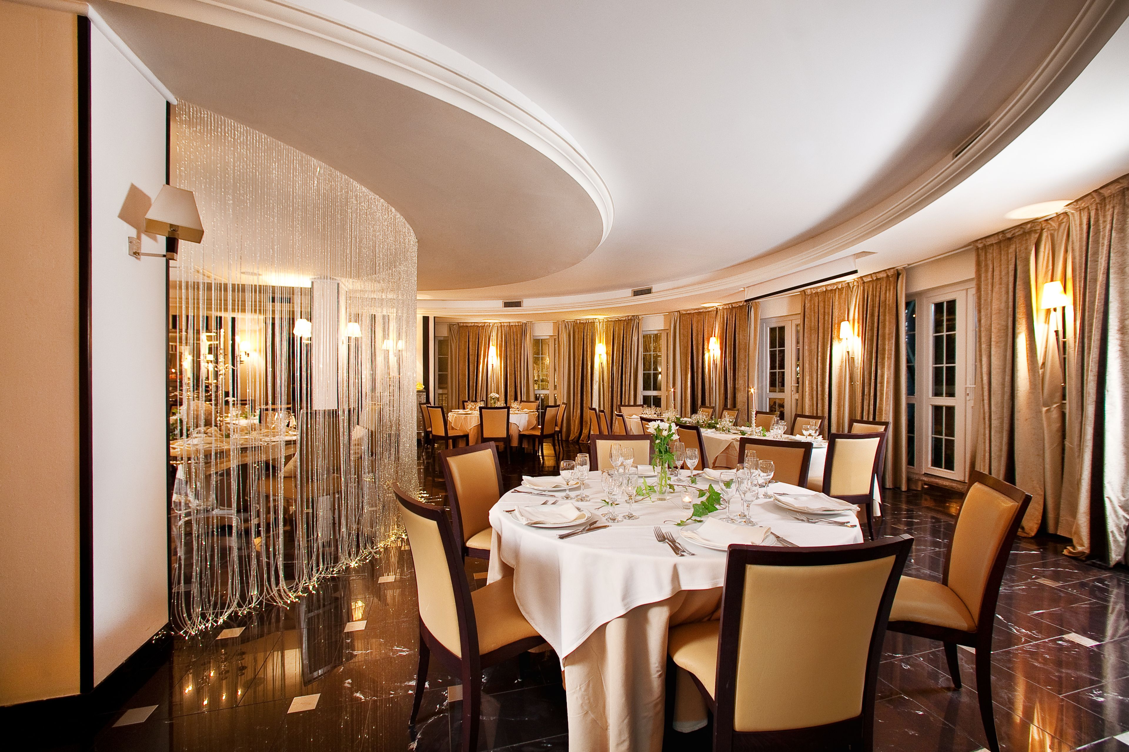 Una sala da pranzo formale con tavoli rotondi, sedie e lampadari.
