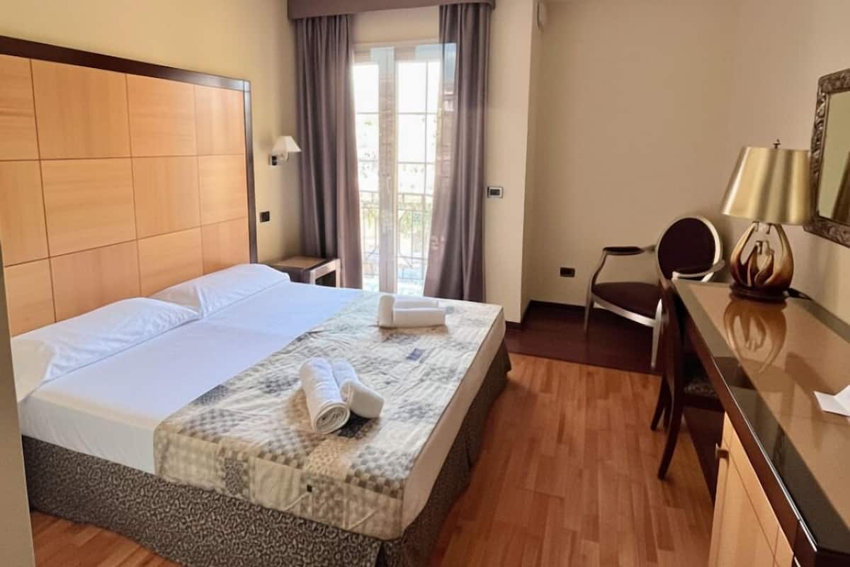 A hotel room with a large bed, a desk, a chair, and a window with curtains.
