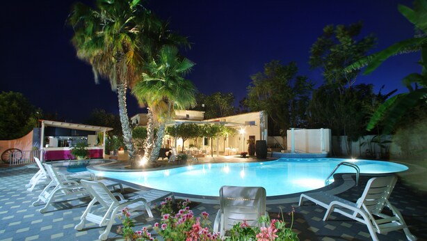 Una piscina con sillas de descanso, una palmera y un edificio con terraza.