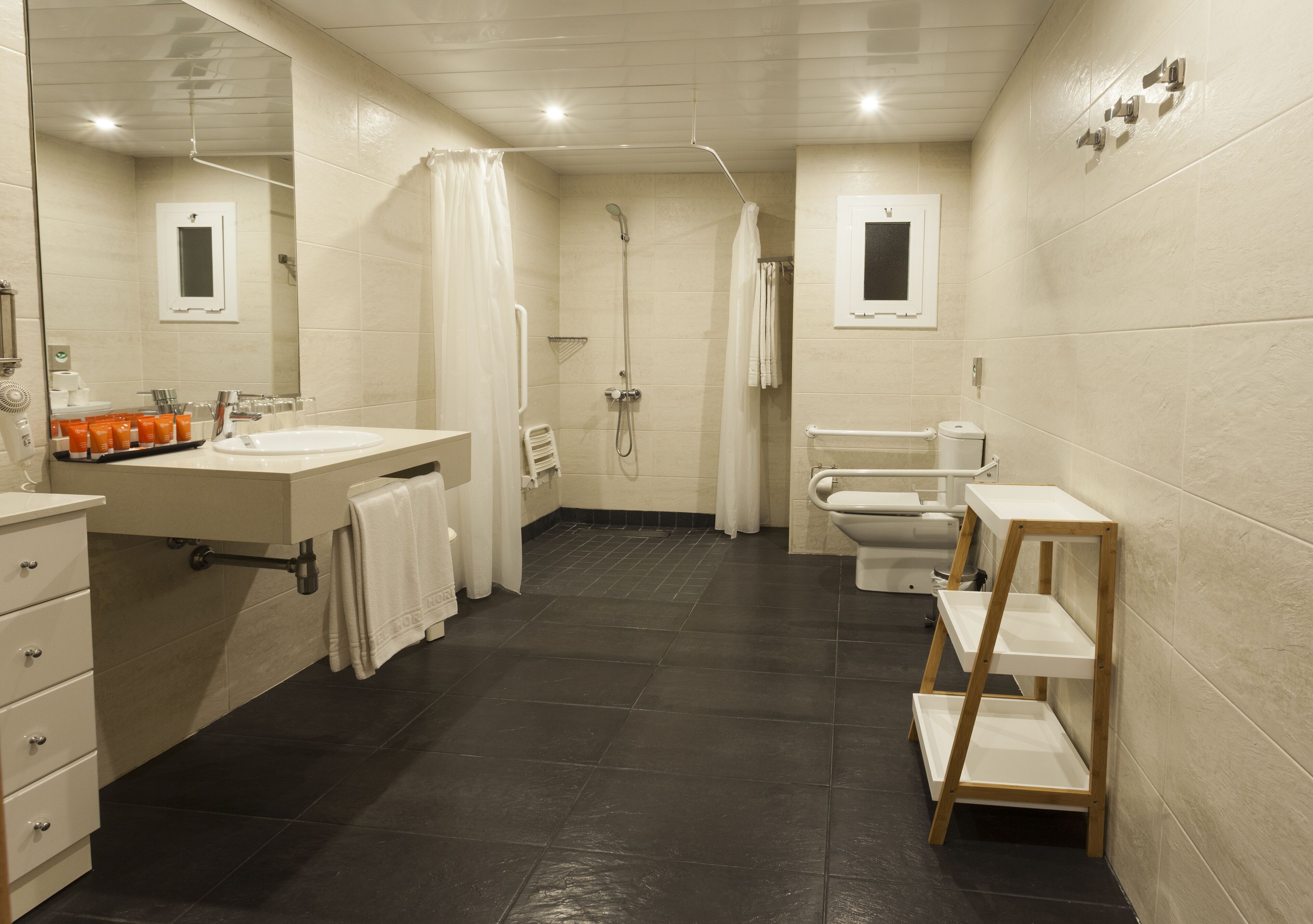 A modern bathroom with a large mirror, a sink, a shower, and a toilet.