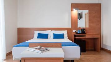 Habitación de hotel con cama, mesita de noche con revista, escritorio con cafetera y espejo.