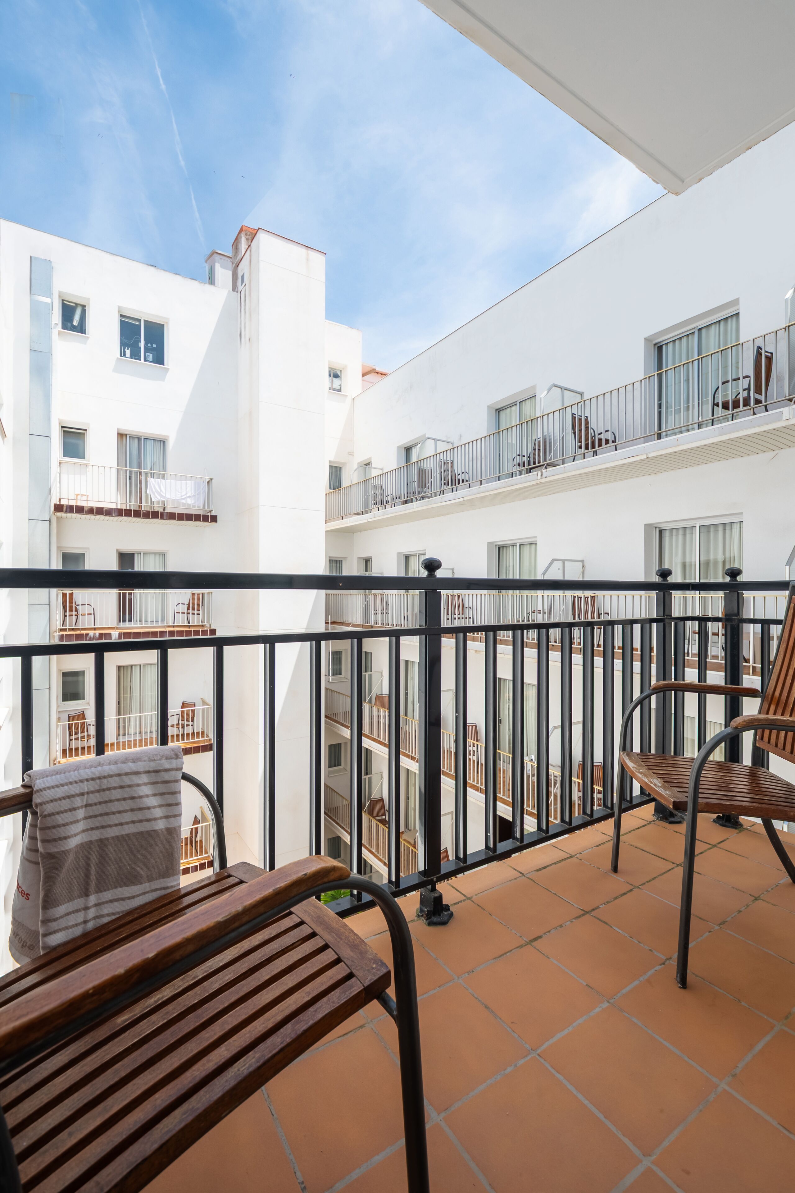 A balcony with a tiled floor, metal railing, and wooden chairs.