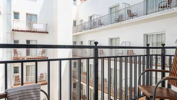A balcony with a tiled floor, metal railing, and wooden chairs.