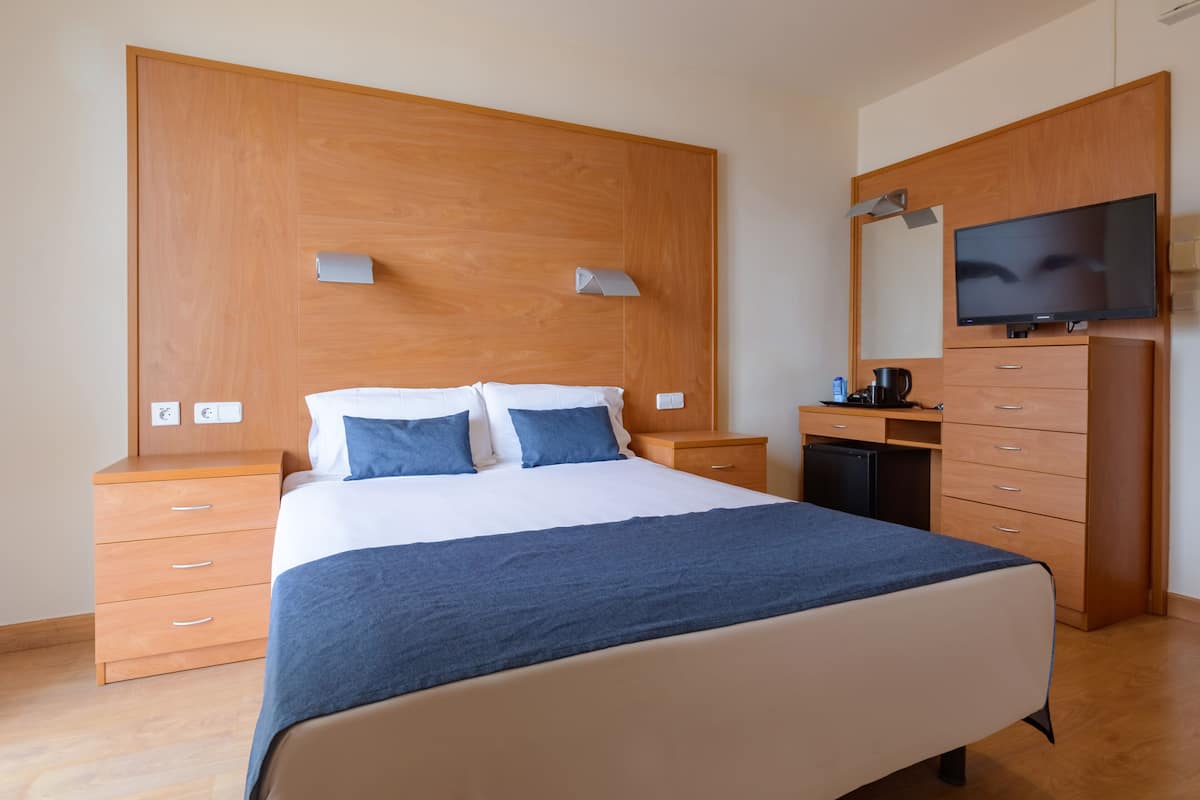 Ein Schlafzimmer mit einem Bett, einem Holz-Kopfteil, Nachttischen, einem Schreibtisch, einem Stuhl, einem Fernseher und einem Kleiderschrank.