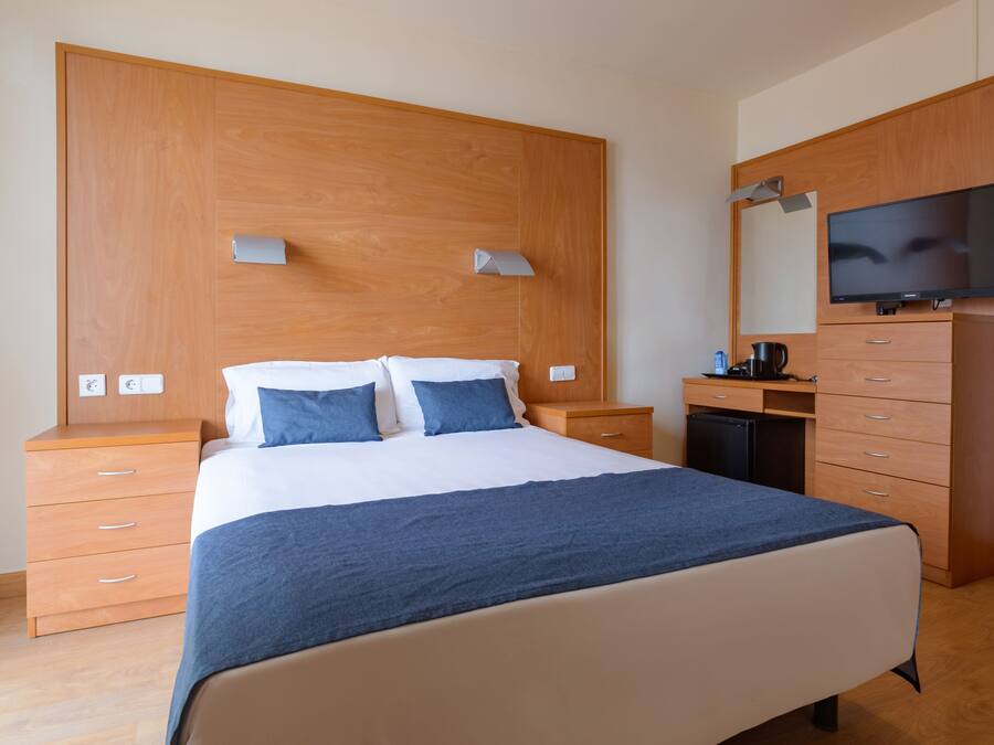 Un dormitorio con cama, cabecera de madera, mesitas de noche, escritorio, silla, televisor y armario.