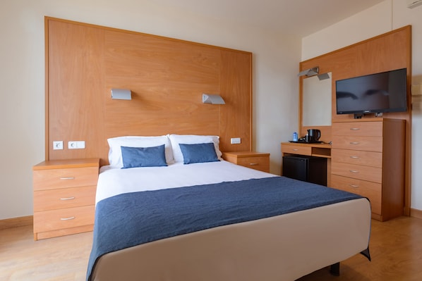 Une chambre à coucher comprenant un lit, une tête de lit en bois, des tables de chevet, un bureau, une chaise, un téléviseur et une armoire.