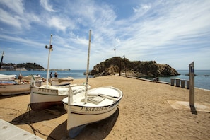 Une plage de sable où sont amarrés plusieurs bateaux, un promontoire rocheux en arrière-plan et un ciel dégagé.
