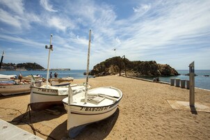 Una playa arenosa con varias embarcaciones amarradas, un promontorio rocoso al fondo y un cielo despejado.
