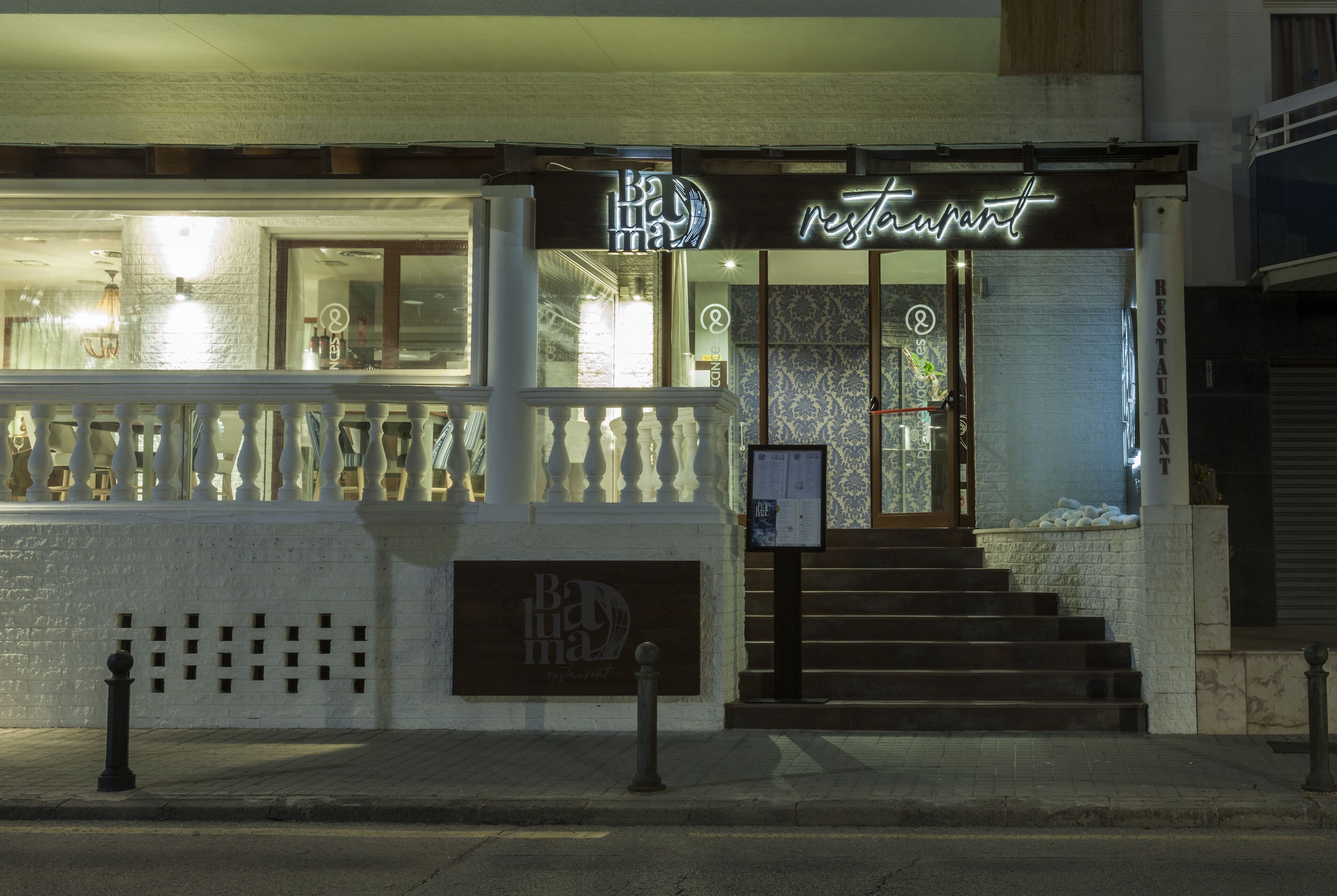 Un restaurante con un letrero de neón, un balcón y una escalera que conduce a la entrada.