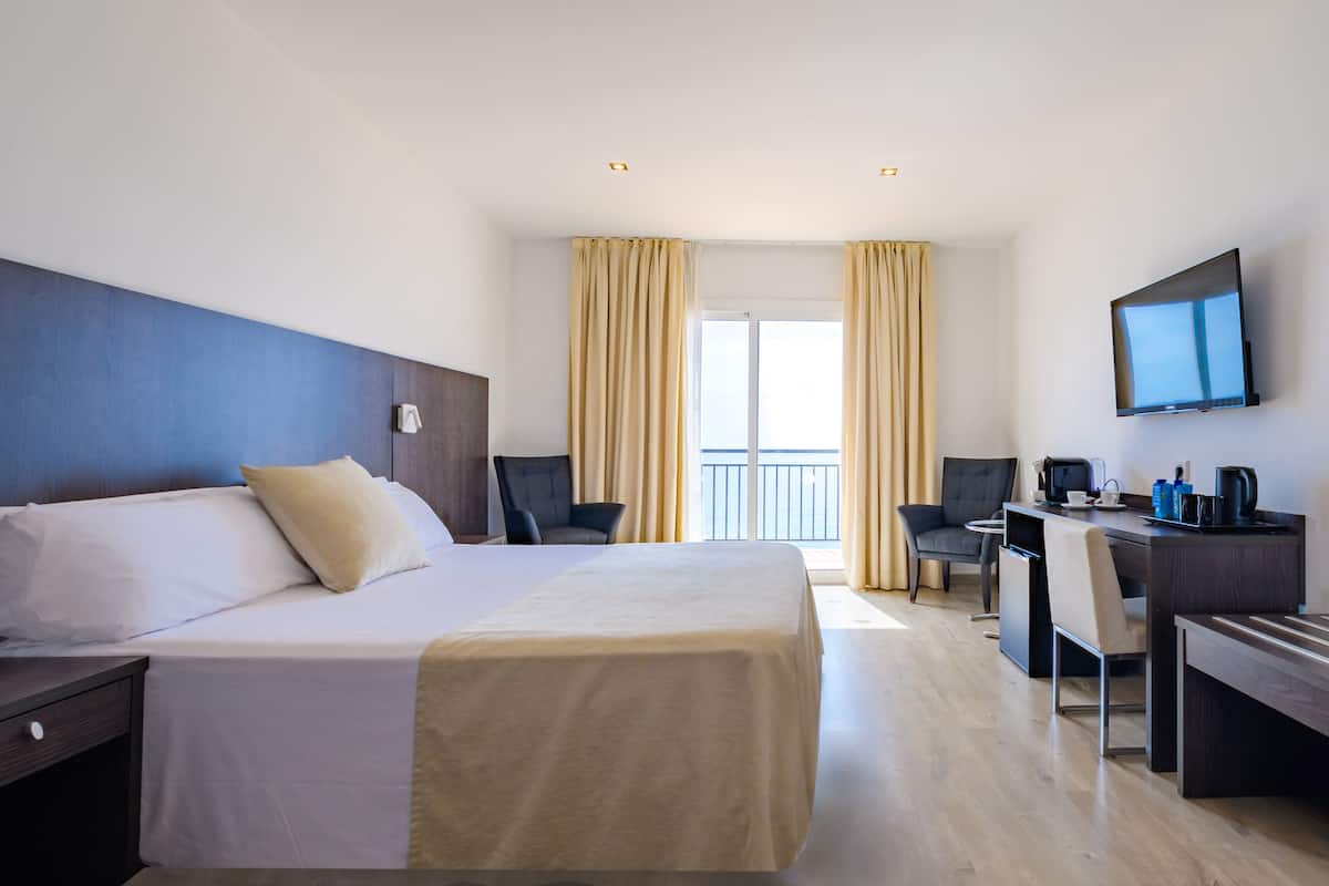 Ein Hotelzimmer mit Bett, Schreibtisch, Stuhl, Fernseher und Vorhängen.