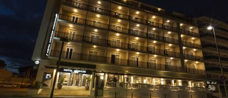 A multi-story hotel with balconies on each floor, a visible entrance, and a street view.