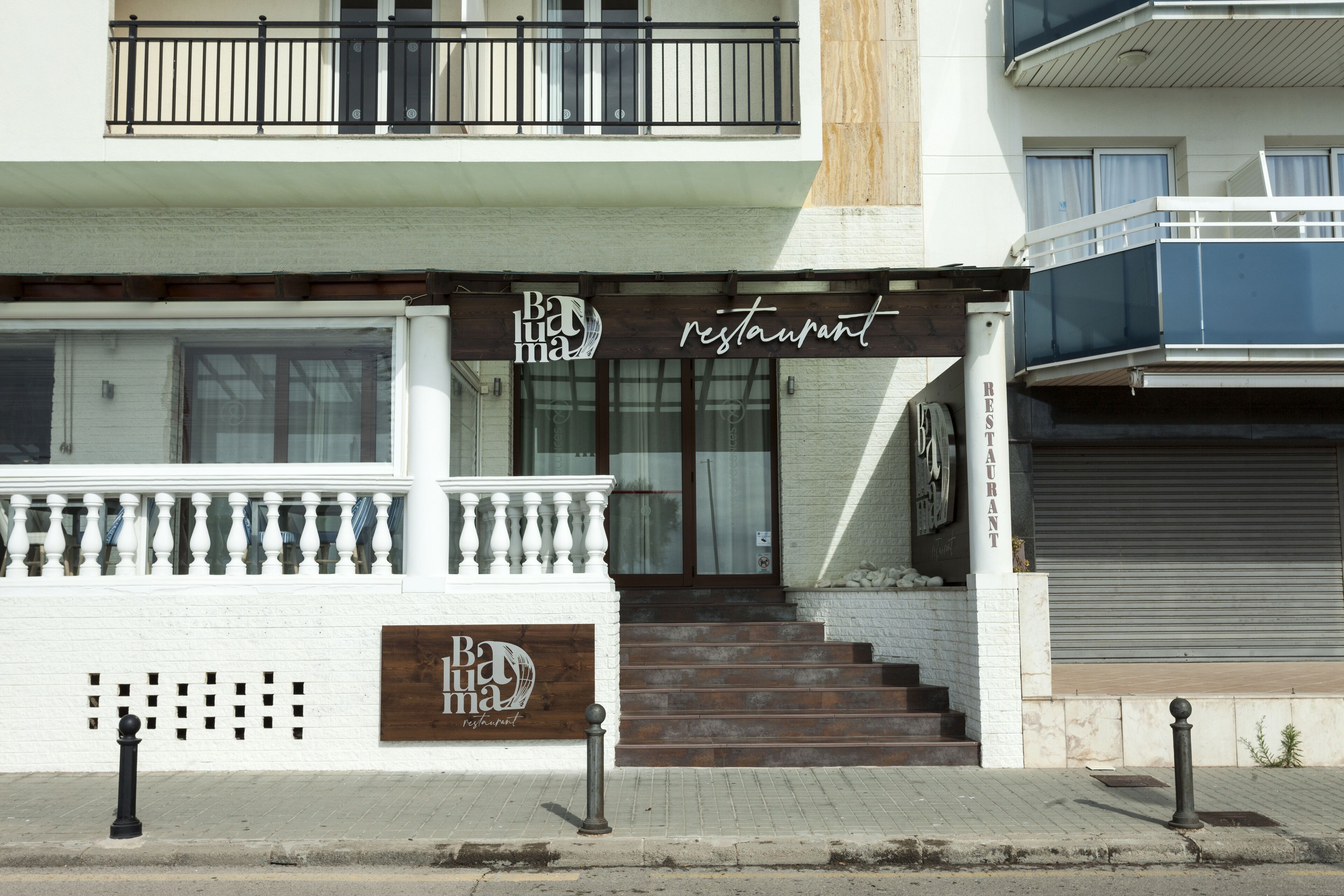 A restaurant with a wooden signboard, a white exterior, and a set of stairs leading to the entrance.