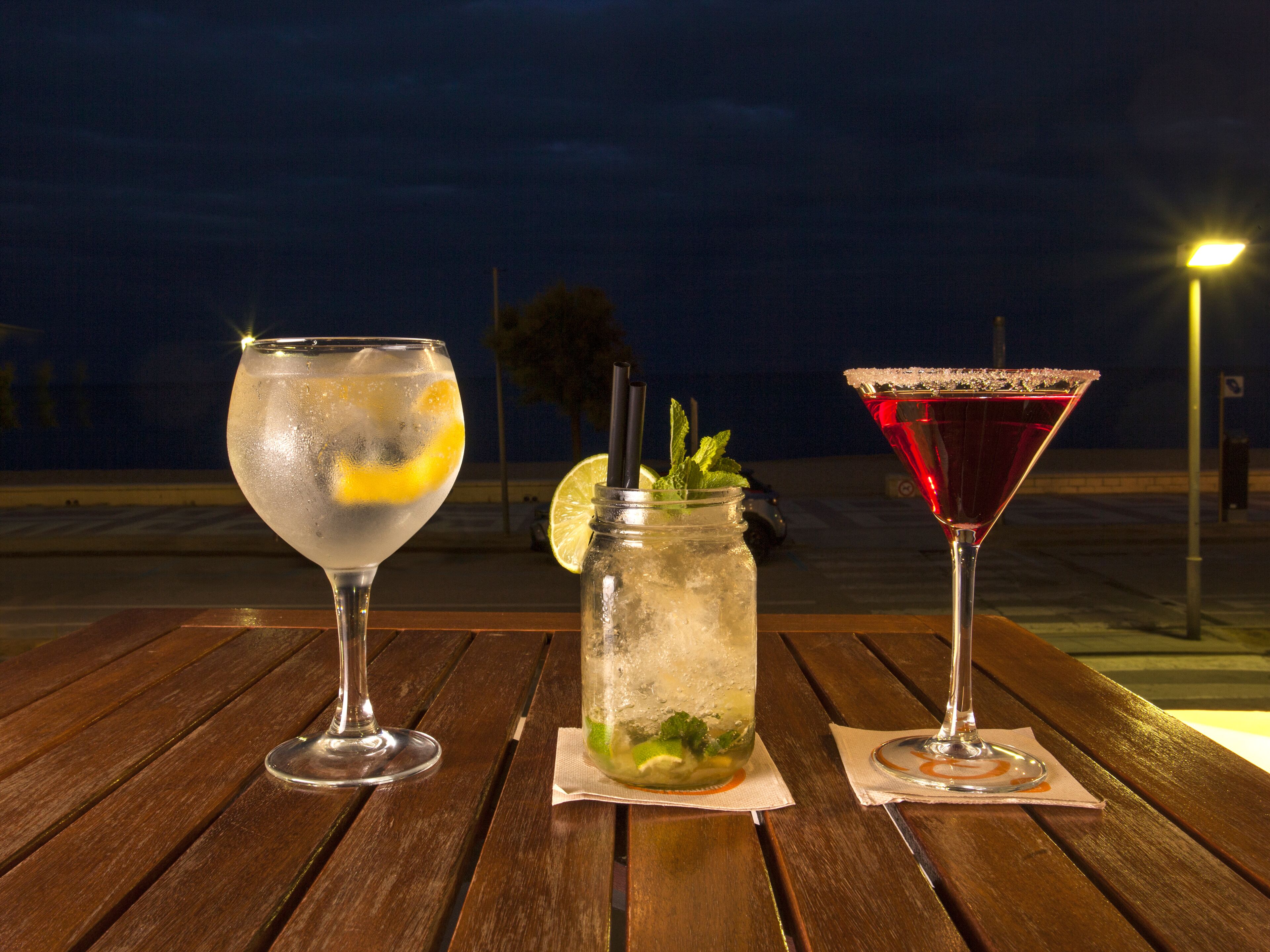 Three drinks on a wooden table with a night sky background.