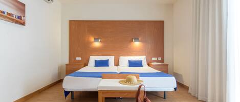 Une chambre d’hôtel avec un lit double, des tables de chevet, une tête de lit en bois, un climatiseur fixé au mur et une fenêtre avec des rideaux.