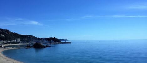 A coastal view with a sandy beach, calm sea, and a rocky outcrop.