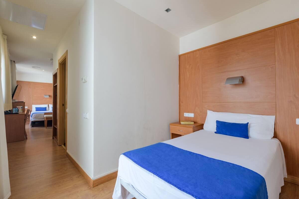 Ein Hotelzimmer mit einem hölzernen Kopfteil, einem Bett mit weißer und blauer Bettwäsche, einem Nachttisch aus Holz und einem Schreibtisch mit Stuhl.