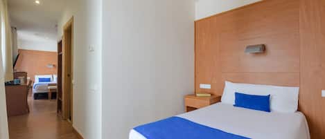 A hotel room with a wooden headboard, a bed with white and blue bedding, a wooden nightstand, and a desk with a chair.