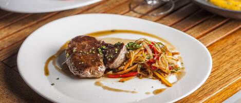A plate of food with a steak and vegetables on a wooden table.