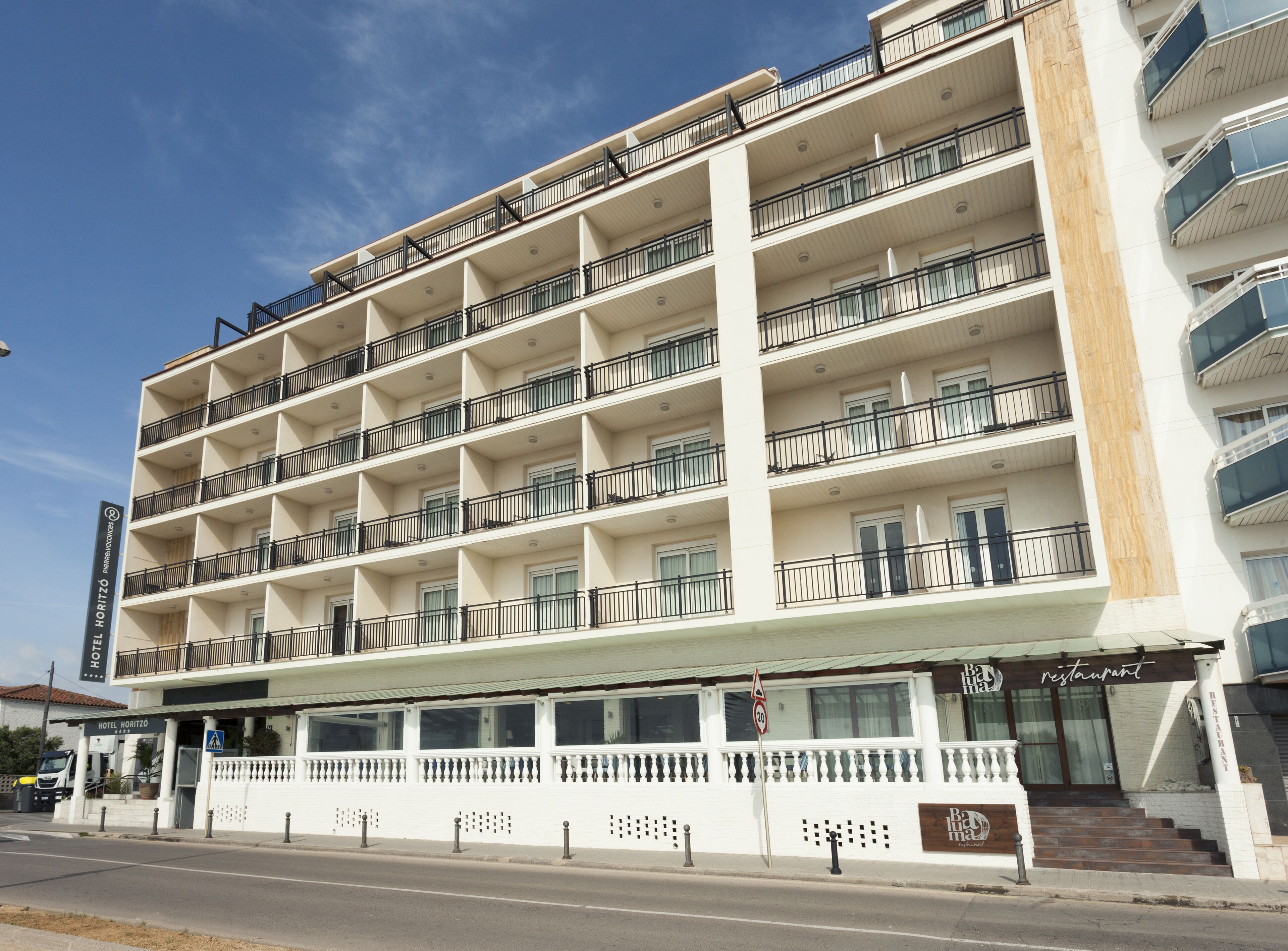 A multi-story hotel with balconies, a restaurant on the ground floor, and a clear sky.