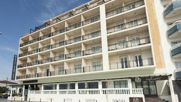 Un hotel de varios pisos con balcones, un restaurante en la planta baja y un cielo despejado.