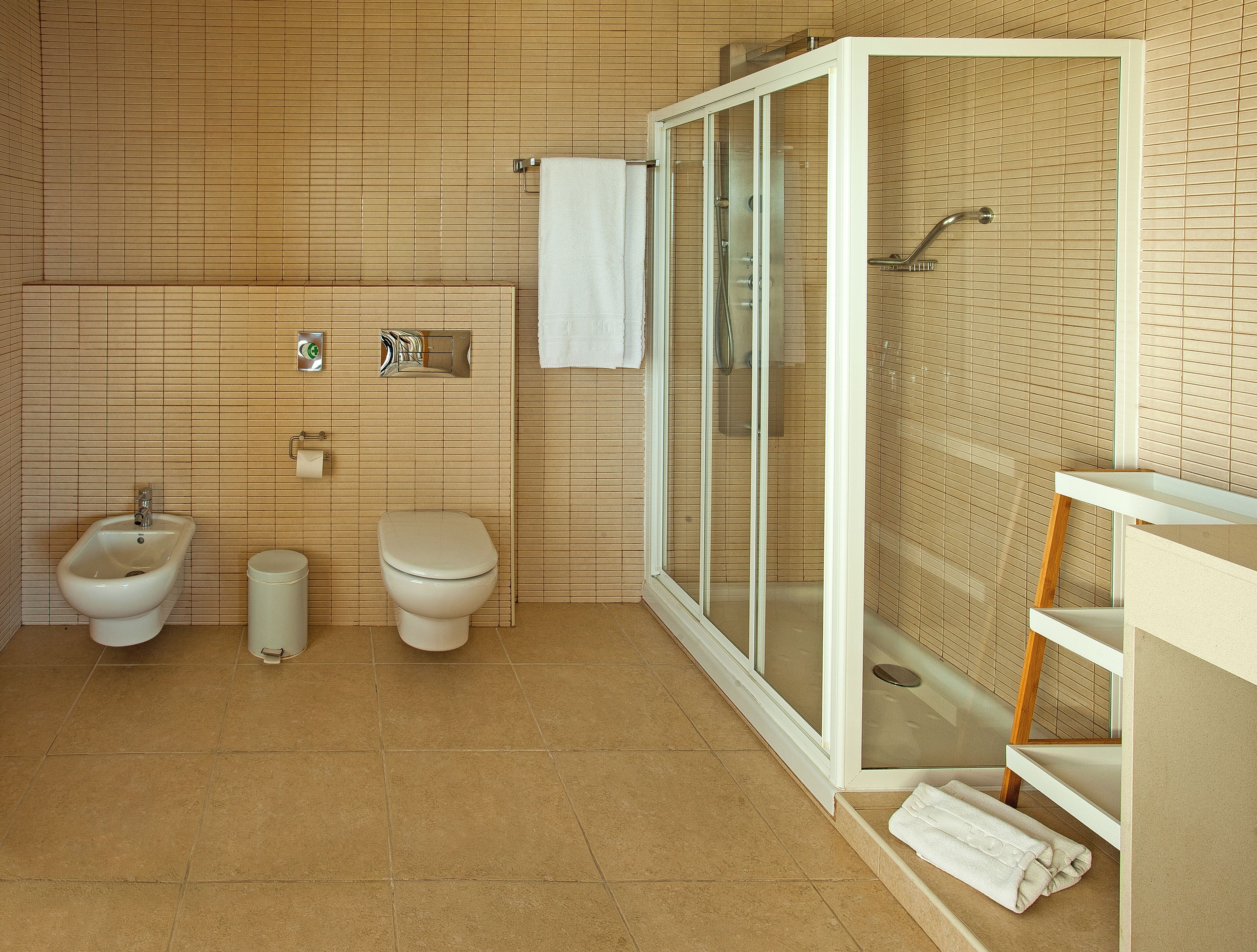 Et badeværelse med bidét, toilet og en brusekabine med glasvægge.