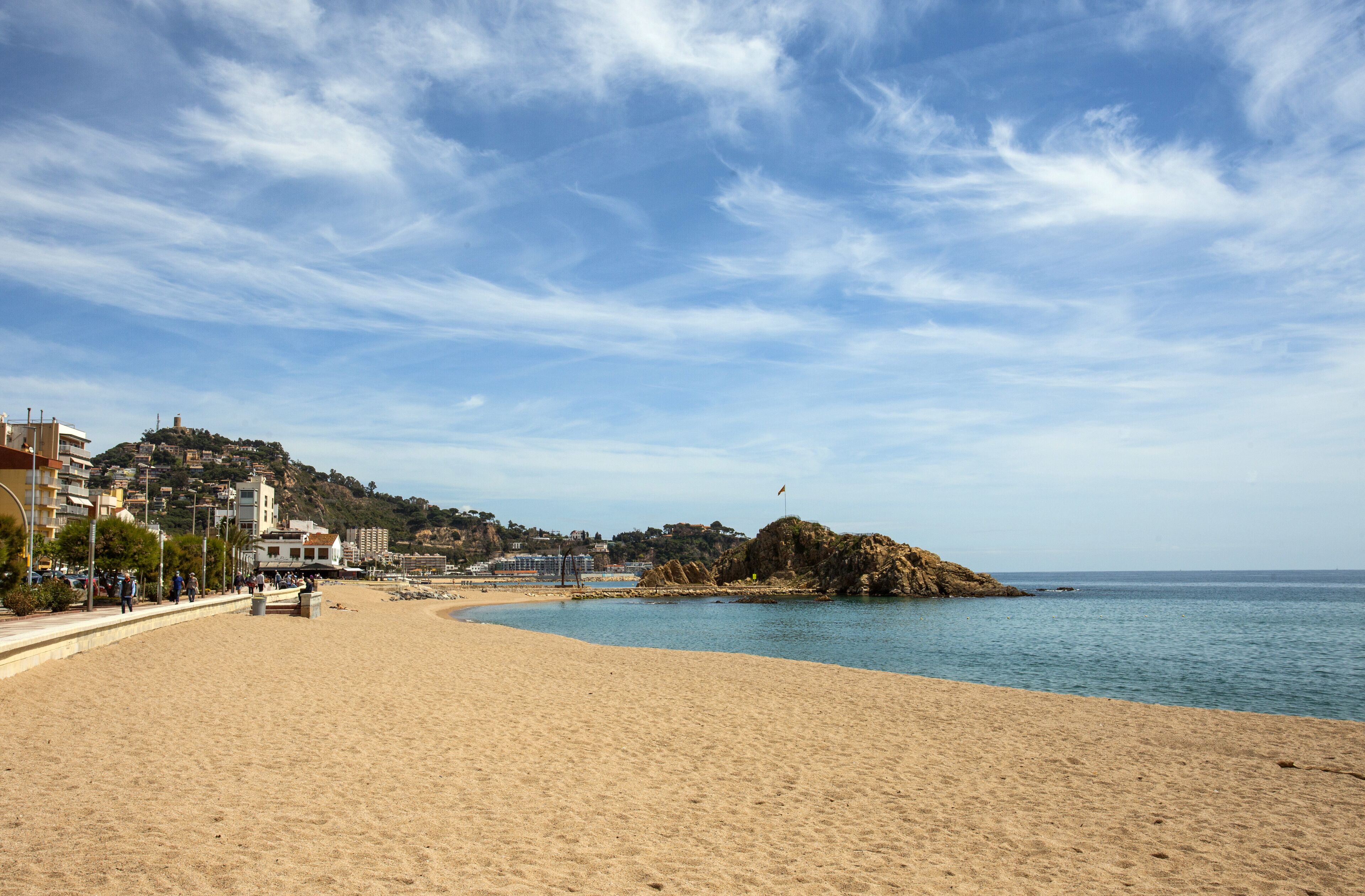 A beach with a sandy shore, a clear sky, and buildings in the background.