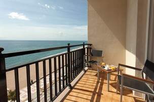 Un balcón con vista al mar, una mesa con una silla y una mesita con una botella y vasos.