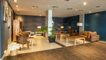 Una sala moderna con un sofá, sillones y una mesita de centro. Hay plantas en macetas y una lámpara.