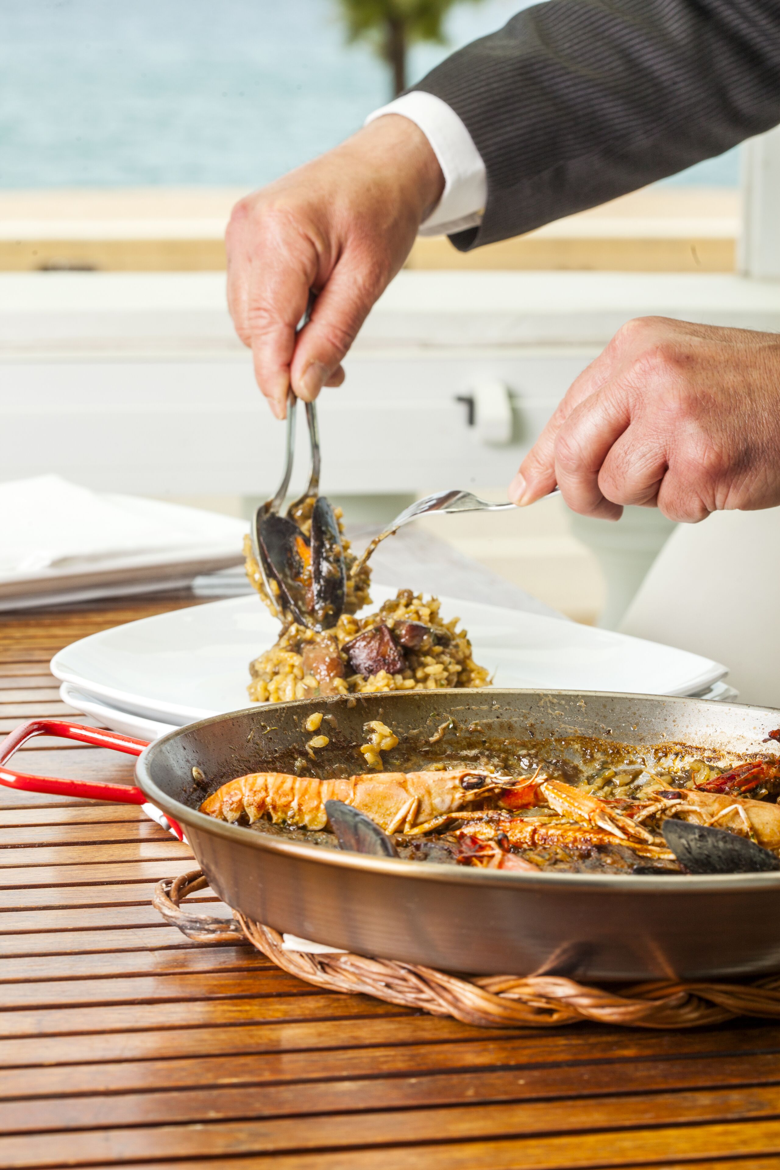 A person serving a dish from a pan on a wooden table.
