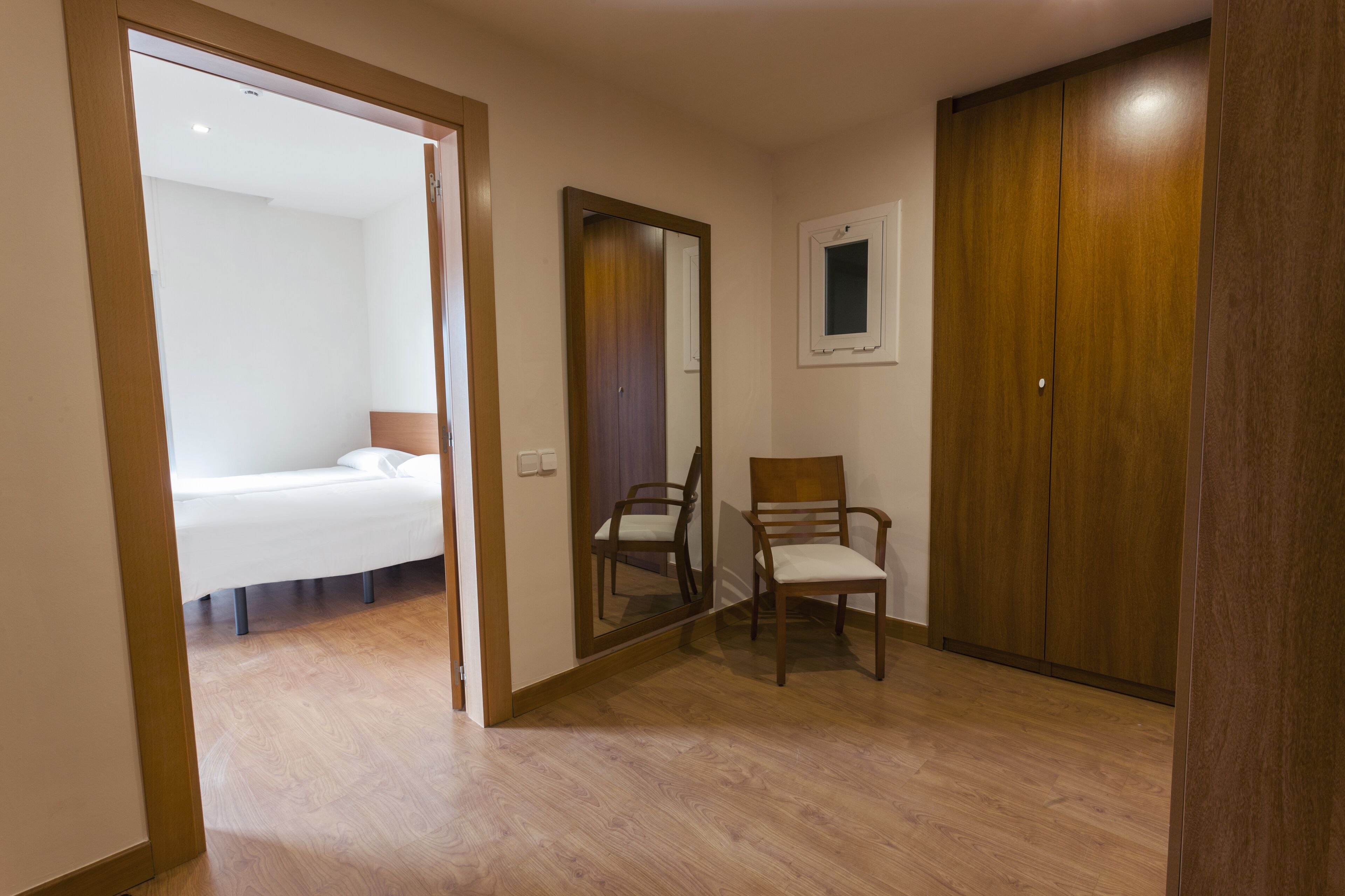A room with a bed, a chair, a wardrobe, and a mirror.