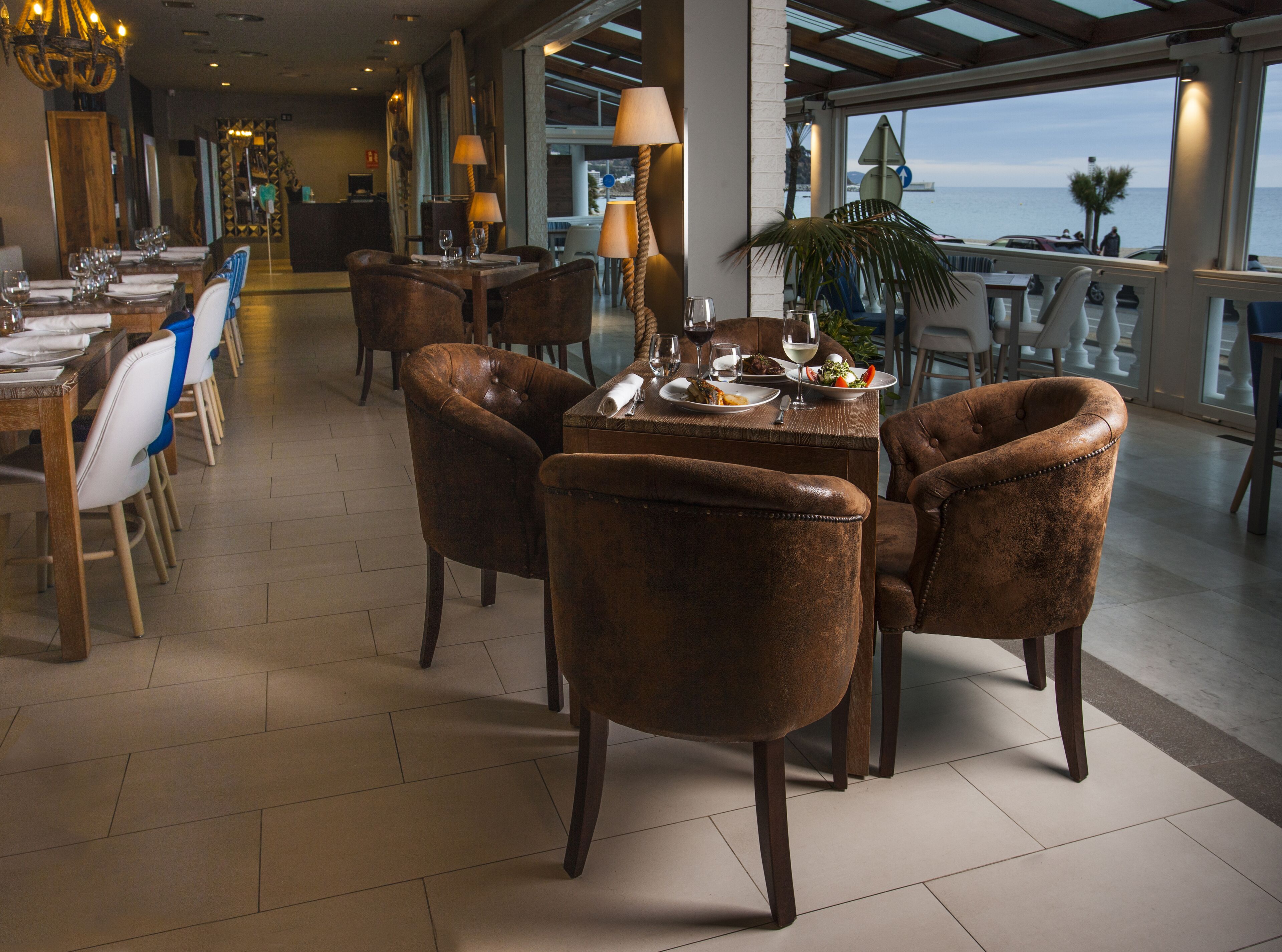 A spacious dining area with leather chairs, a wooden table set for a meal, and a view of the sea through large windows.