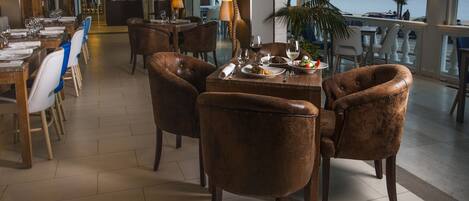 A spacious dining area with leather chairs, a wooden table set for a meal, and a view of the sea through large windows.
