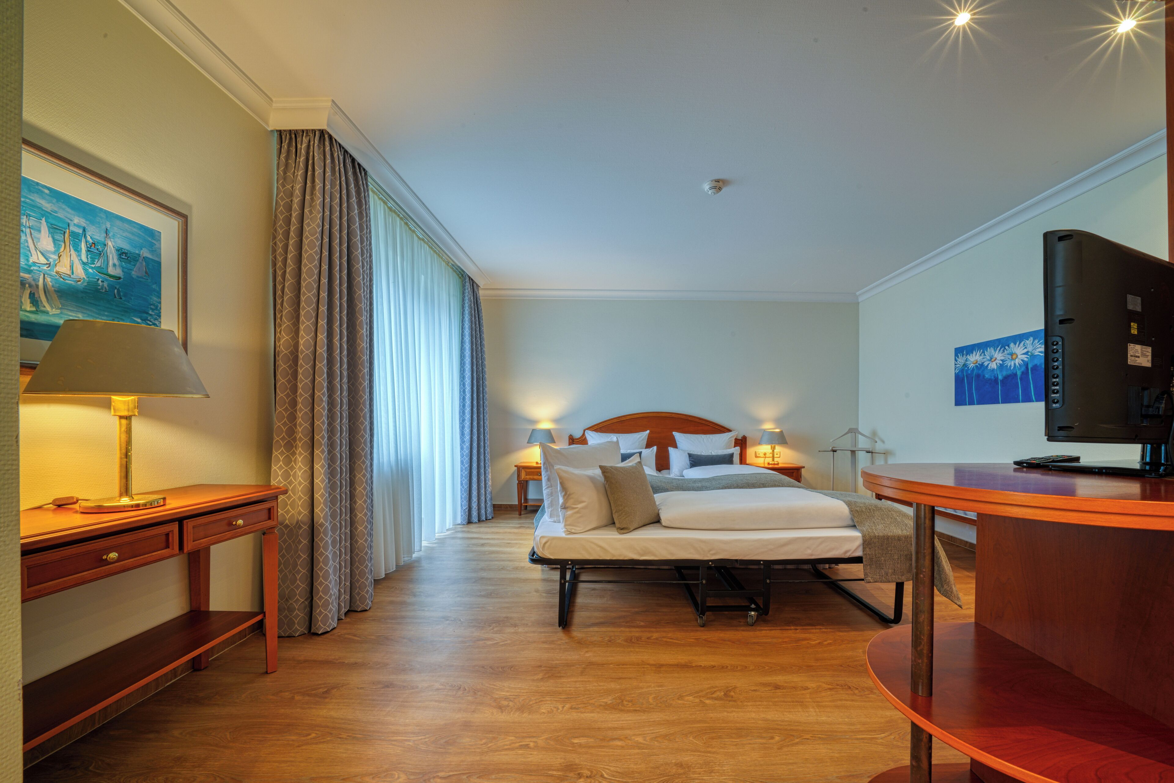 Ein Hotelzimmer mit einem Bett, Nachttischen, einem Schreibtisch, einem Fernseher und Kunstwerken an den Wänden.