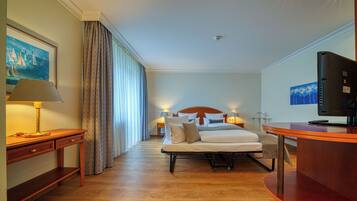 Ein Hotelzimmer mit einem Bett, Nachttischen, einem Schreibtisch, einem Fernseher und Kunstwerken an den Wänden.