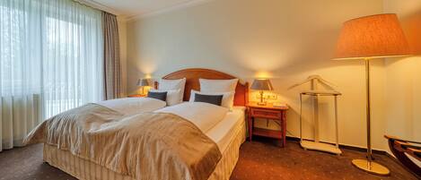 A hotel room with a large bed, two bedside tables with lamps, a floor lamp, and a bench.