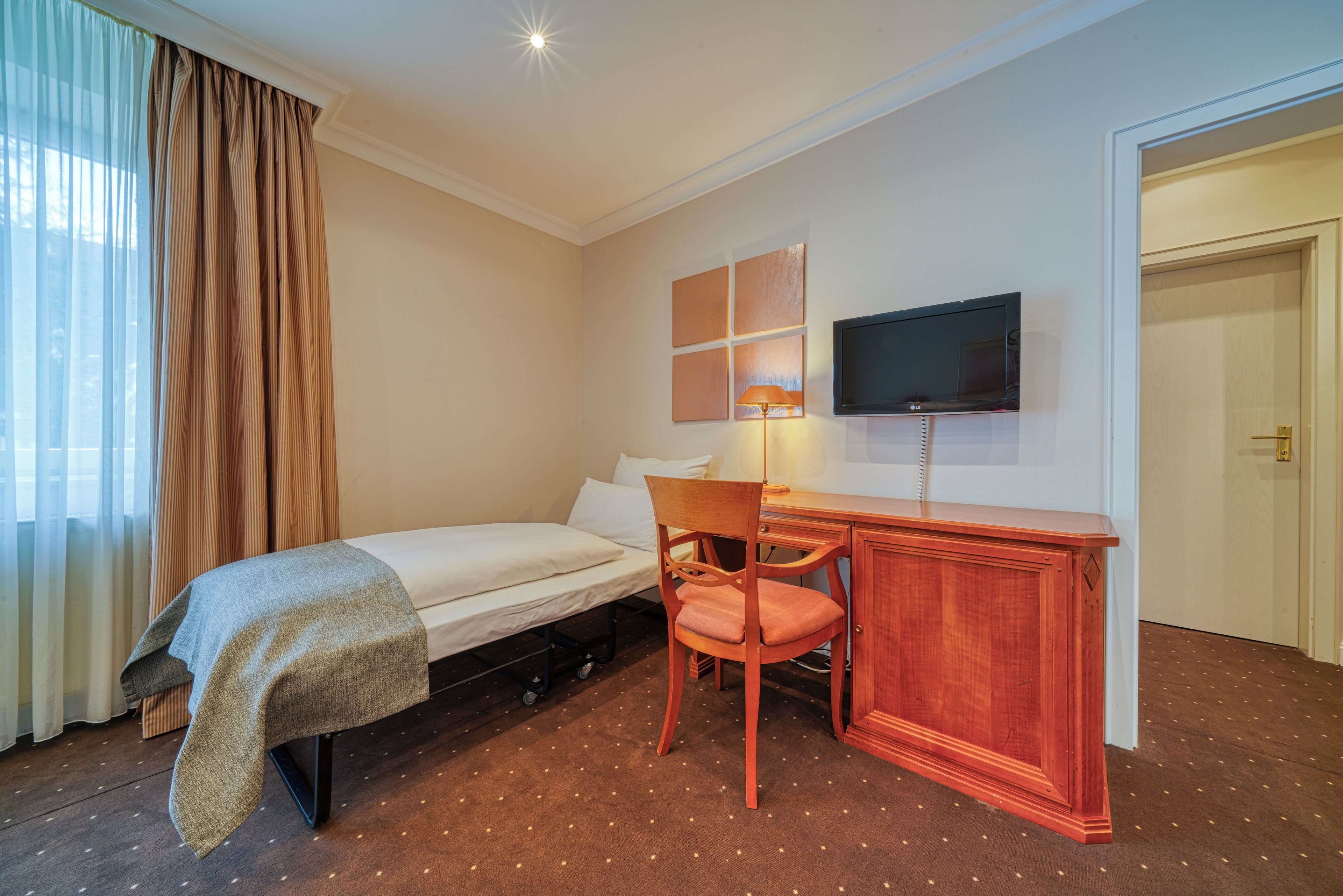 A hotel room with a bed, a desk, a chair, a television, and a window with curtains.