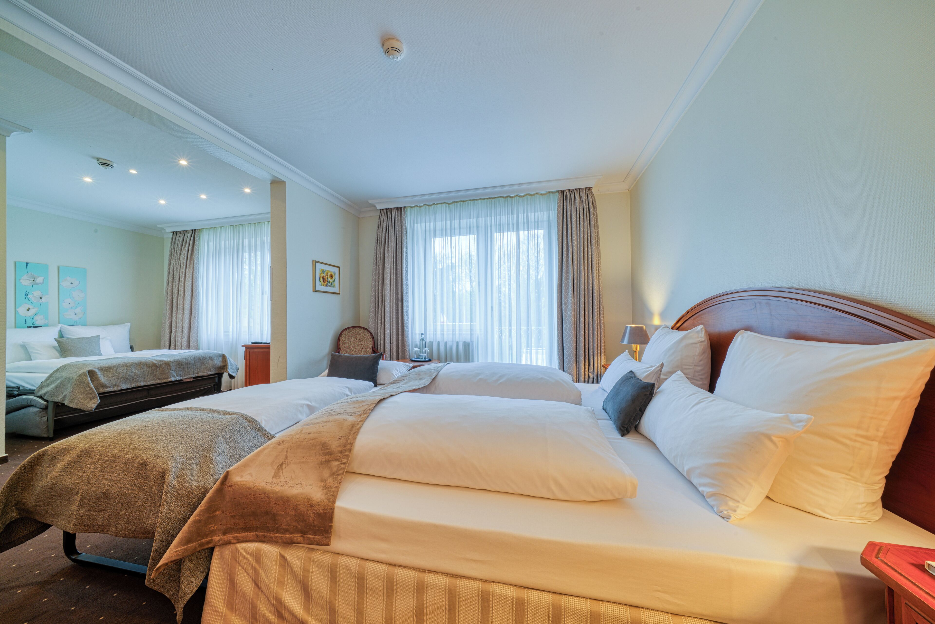 A hotel room with two beds, a large window with curtains, and a small table with a lamp.