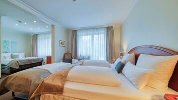 A hotel room with two beds, a large window with curtains, and a small table with a lamp.