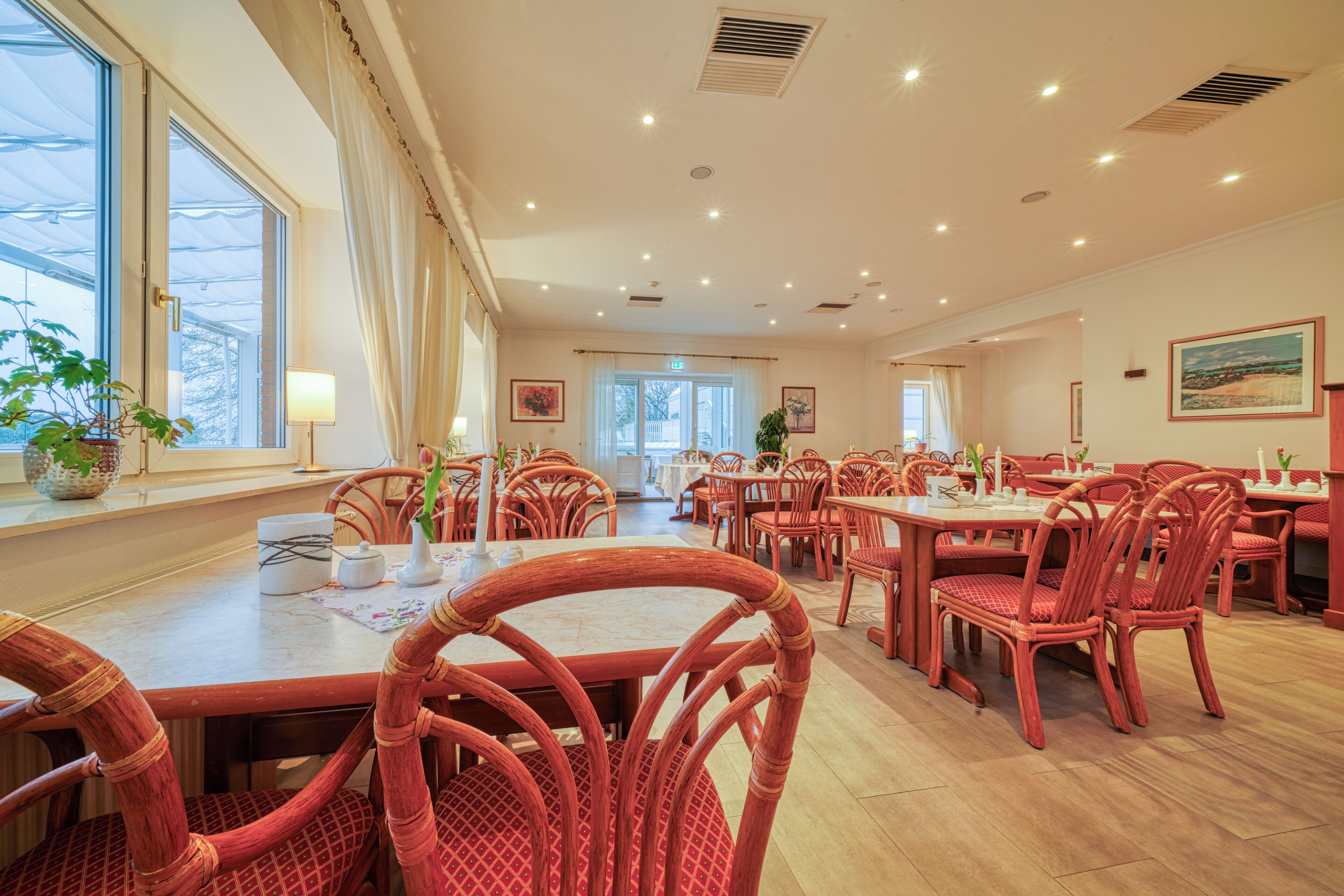 A spacious dining area with high ceilings, multiple tables and chairs, and large windows allowing natural light.