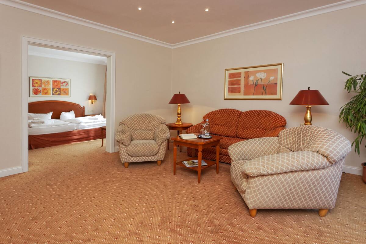 Une chambre d’hôtel comprenant un lit, deux fauteuils, une petite table et deux lampes.