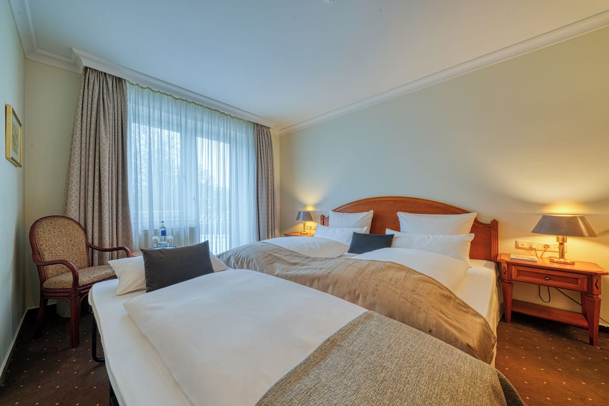 Une chambre d’hôtel avec deux lits, une chaise, une table de chevet avec une lampe et une fenêtre avec des rideaux.