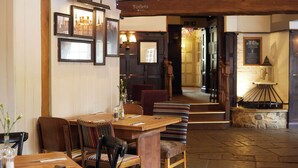 Een restaurantinterieur met houten tafels en stoelen, foto's in lijsten aan de muur en een bordje dat de weg naar de toiletten wijst.