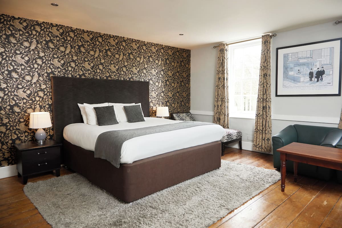 Une chambre avec un grand lit, deux tables de chevet avec des lampes, un canapé vert, une table basse en bois et un papier peint à motifs.