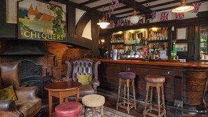 Een bar met een houten toonbank, krukken, een open haard en een muurschildering.