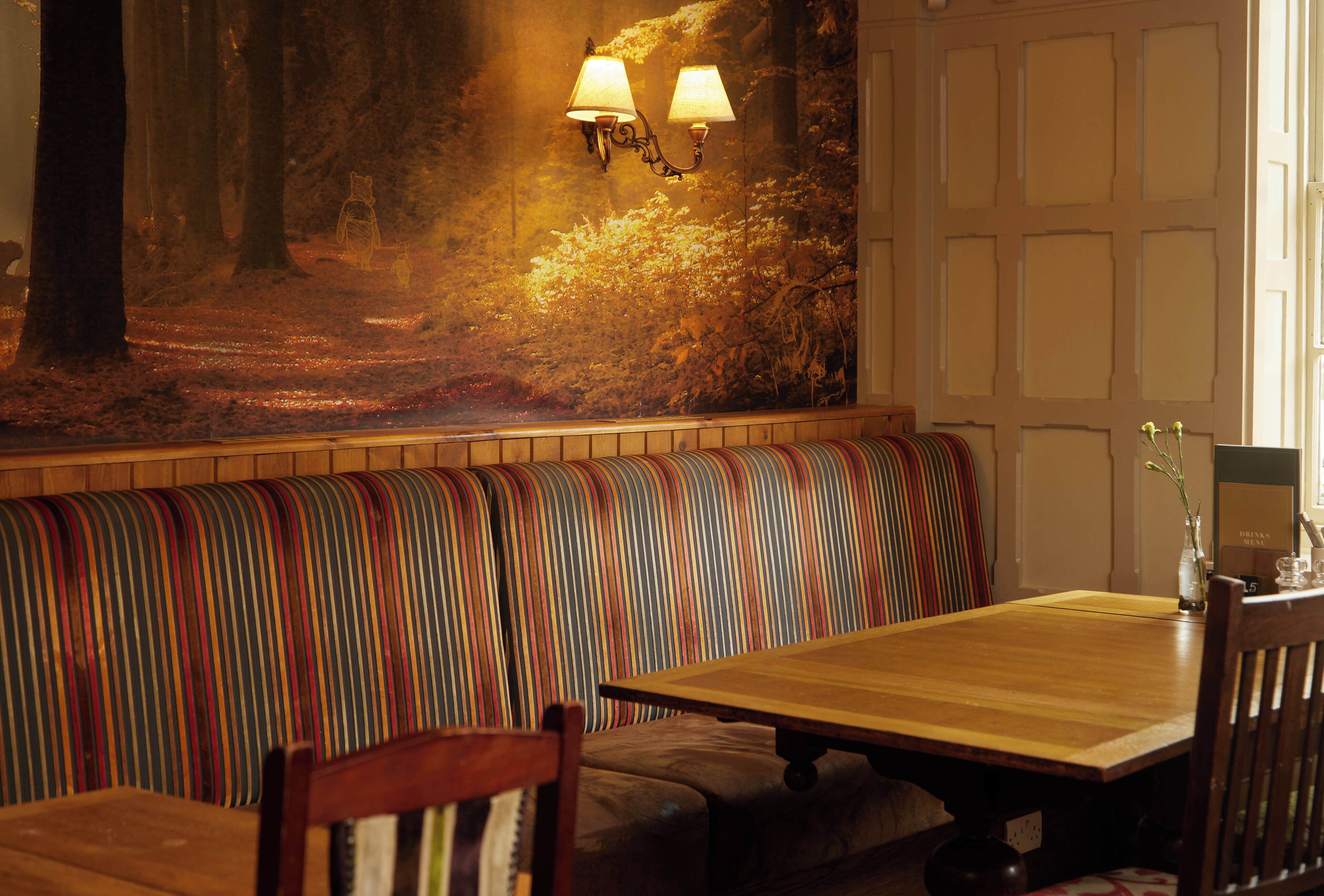 Un restaurant avec des tables et des bancs en bois, une fresque représentant une scène de forêt et des lampes fixées aux murs.