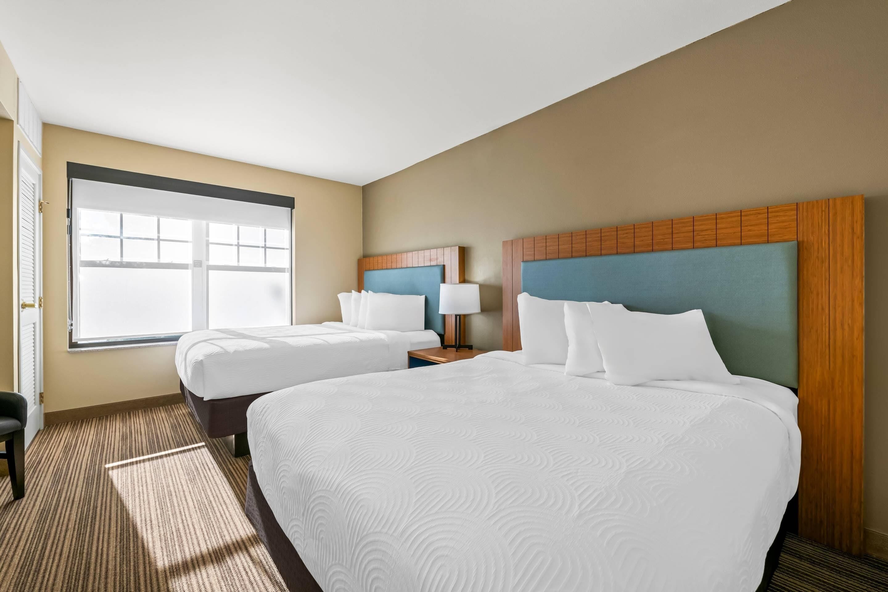 A hotel room with two beds, a large window, a desk, and a chair.
