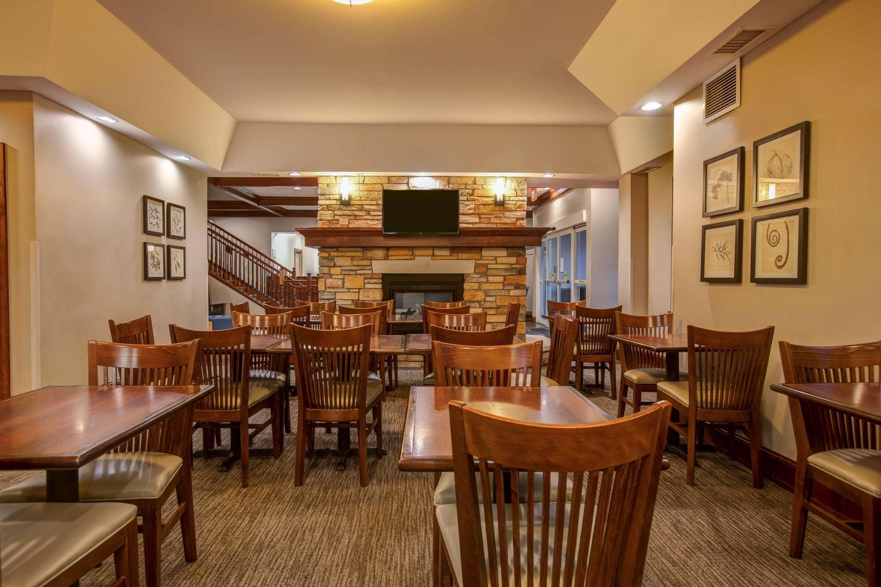 A dining area with wooden tables and chairs, a stone fireplace, and a television mounted above it.