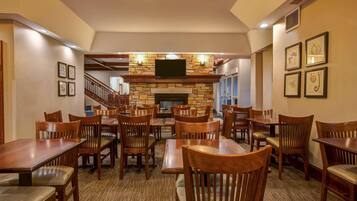 A dining area with wooden tables and chairs, a stone fireplace, and a television mounted above it.